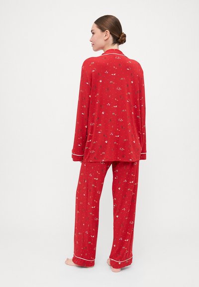 Conjunto de pijama estampado em vermelho, com uma parte de cima de botões de mangas longas e calças combinantes, com acabamento em branco e tecido com um caimento descontraído.