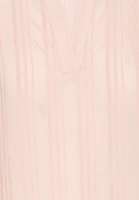 Tunique rose pâle avec un col en V, présentant des rayures verticales et un tissu texturé. Le design est de coupe décontractée avec des détails de coutures subtiles.