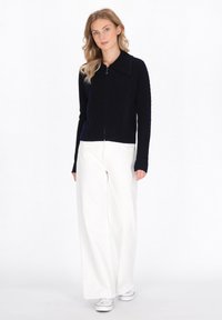 Cardigan zip-up blu navy con texture a coste e colletto ampio, abbinato a pantaloni bianchi a vita alta e larghi e sneakers bianche.