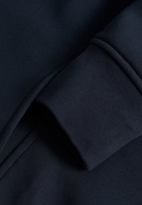 Sudadera de un oscuro tono navy con una textura suave y puños acanalados. El diseño tiene un aspecto minimalista y casual, sin patrones visibles.