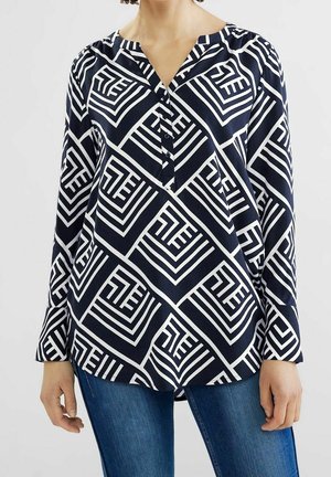 Blouse marine à motif géométrique blanc, avec un col en V et une patte de boutonnage, des manches longues et une coupe décontractée. Tissu texturé.