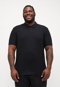 Sort polo shirt med tekstureret stof, korte ærmer og en tre-knaps lukning. Har en let krave og diskret logodetalje.