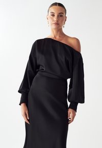 Čierne saténové šaty s dizajnom bez ramienok, dlhými vypnutými rukávmi a naťahovacími manžetami. Hladká textúra, priliehavá silueta a jednofarebný vzhľad.