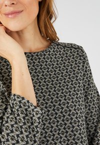 Top nero e grigio a fantasia con collo rotondo e maniche a tre quarti, tessuto testurizzato con disegni geometrici in tonalità sottili.