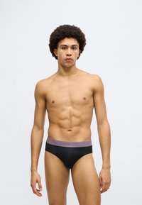 Fekete férfi alsónadrág lila derékpánttal, melyen a „Schiesser” márkanév kontrasztos színben látható. Simább anyagból készült, testhez álló szabással.