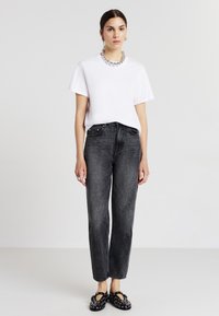 T-shirt bianco in cotone, vestibilità comoda; jeans neri a vita alta, gamba dritta; ballerine nere a motivo; collana argentata spessa; stile minimalista.