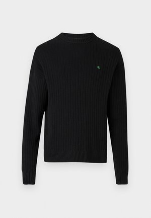 Suéter negro acanalado con mangas largas, cuello alto y pequeño logo verde en el pecho. Textura suave, corte casual.