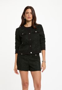 Svart tweedjacka med accenter av silvertråd, med rundad krage, framfickor och silverknappar, matchad med shorts i samma material.