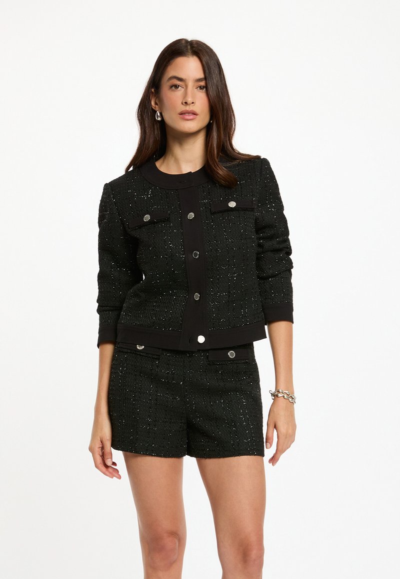 Svart tweedjacka med accenter av silvertråd, med rundad krage, framfickor och silverknappar, matchad med shorts i samma material.