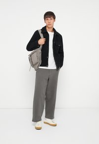 Sort jakke over en hvid skjorte, grå brede bukser, hvide sneakers med beige såler og en grå skuldertaske med lynlåse. Enkel design, moderne udseende.
