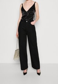 Svarta vida byxor med en strukturerad yta prydd med små glittrande detaljer, kombinerat med en svart satin-V-ringad topp och stiletto-klackar.