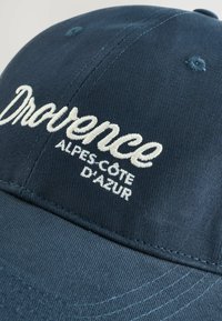 Căciulă de baseball bleumarin, cu text brodat alb care spune "Drocence Alpes-Côte d'Azur" pe panoul din față.