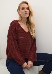Bordový pletený sveter s voľným strihom, s výstrihom do V a textúrovaným otvoreným vzorom. Doplnkovaný rebrovaným lemom a manžetami.