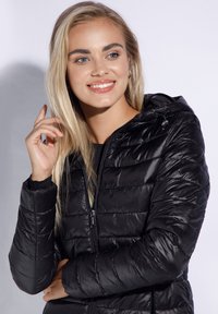 Zwarte pufferjack met quilted textuur, capuchon en ritssluiting. Gemaakt van glanzend materiaal, met elastische manchetten en een verstelbaar trekkoord.