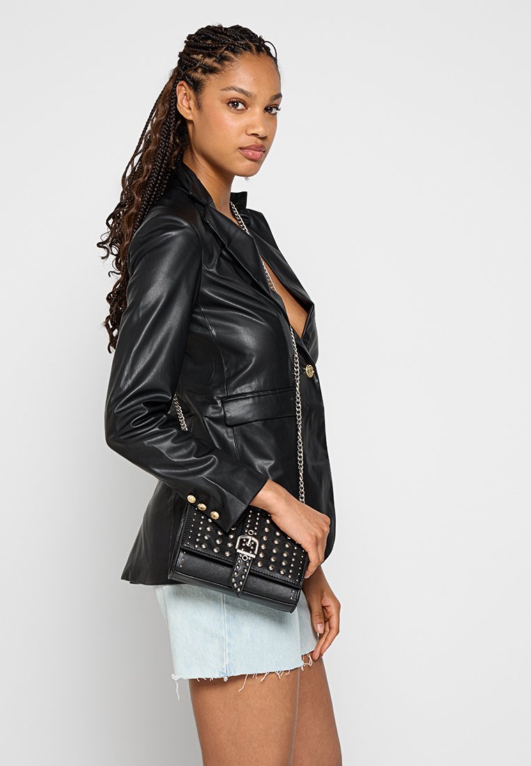 Blazer in similpelle nera con una vestibilità sartoriale, caratterizzato da rever a lancia e dettagli in bottone dorato. Abbinato a una borsa nera con borchie.