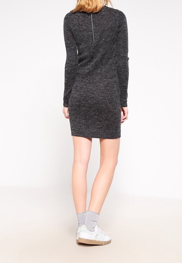 Abito lungo grigio scuro a maniche lunghe con design aderente e zip sul retro. Il modello indossa sneaker bianche e calzini grigi. Tessuto morbido e testurizzato.