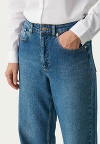 Modre denim hlače z udobnim krojem in srednjim pasom, z obliko petih žepov in vidnimi šivi.