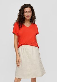 Rode V-hals t-shirt van een zachte stof, gecombineerd met een beige linnen rok met een elastische tailleband en zijzakken.