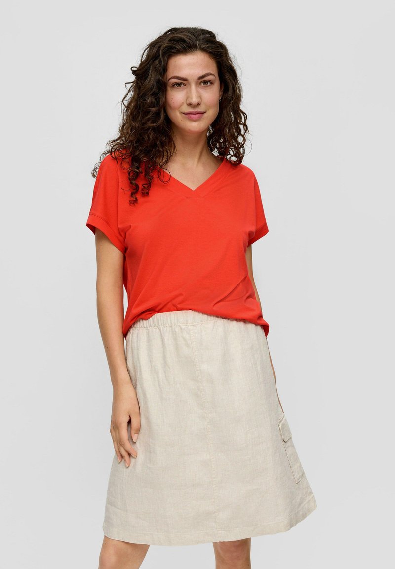 Rotes V-Ausschnitt-T-Shirt aus weichem Stoff, kombiniert mit einem beigen Leinenrock mit elastischem Taillenbund und seitlicher Tasche.