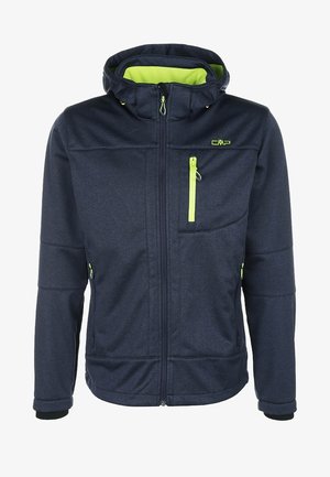 Homme marchant portant une veste bleu marine avec doublure jaune fluo, chemise grise, pantalon cargo noir et chaussures de randonnée noires.