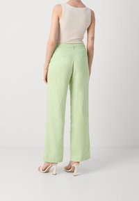 Světle zelené lněné široké kalhoty s dvěma zadními kapsami a vysokým pasem, doplněné krémovými sandály na podpatku.