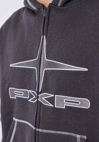 Sudadera gris con cremallera hecha de tela suave, que presenta un gran gráfico de estrella blanca y la inscripción "PXP" en el pecho, con detalles de costura en contraste.