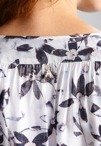 Gros plan d'un décolleté dos avec un tissu floral noir et blanc et un petit charm en forme d'abeille en argent suspendu au col.