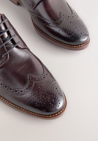 Chaussures habillées en cuir marron avec un design brogue, présentant des détails perforés, une finition polie et un bout arrondi.