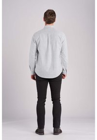 Koszula na guziki w paski w jasnoniebieskim i białym kolorze, z długimi rękawami i zaokrąglonym dołem, zestawiona z czarnymi, dopasowanymi jeansami i szarymi butami.