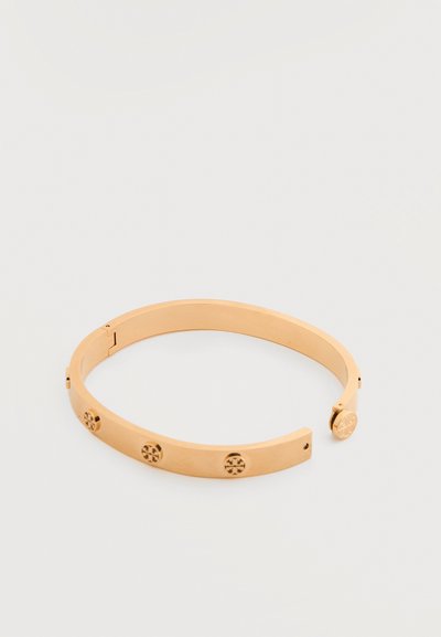 Βραχιόλι-μανσέτα από μέταλλο με επίστρωση σε χρυσό τόνο, διακοσμημένο με στρογγυλά σήματα λογοτύπου ομοιόμορφα κατανεμημένα κατά μήκος της στεφάνης του, με ανοιχτό άκρο.