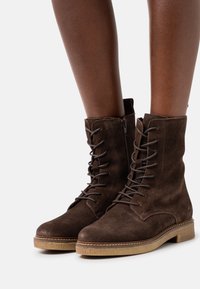 Stivaletti alla caviglia in suede marrone, con lacci davanti, chiusura con zip laterale, punta rotonda e suola in gomma texturizzata.