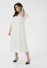 Vit broderad midiklänning med korta puffsärmar, ögla-textur och V-ringning. Matchad med svarta klackskor med spänne.
