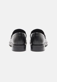 Mocassins en cuir noir avec une finition lisse, bout rond, petit talon empilé, et panneaux élastiques sur les côtés pour un enfilage facile.