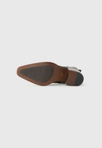 Suela de zapato de cuero con un elegante acabado marrón en la parte superior, talón de goma negra texturizada y diseño curvado. La parte inferior presenta un patrón de relieve para un buen agarre.