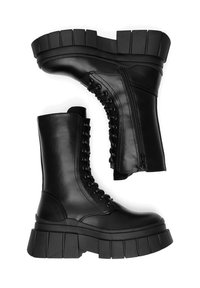 Czarne skórzane buty wojskowe z masywnymi, ryflowanymi podeszwami, sznurowane z przodu i zamkiem błyskawicznym z boku, ustawione z jednym butem w pozycji pionowej, a drugim na boku.