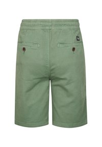 Shorts verts longueur genou avec taille élastique, poches passepoilées à l'arrière avec bouton, et une petite étiquette de marque noire sur le côté droit.