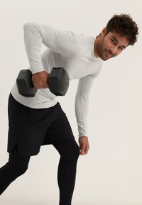 Graues langärmliges Sportshirt mit strukturierten Details, schwarze Shorts und schwarze Hanteln. Die Figur ist in einer gebogenen Position und führt eine Übung aus.