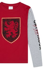 Czerwona koszulka z długim rękawem z emblematem czarnego lwa w złotej ramce z przodu; szare rękawy mają tekst w czerni i czerwieni. Miękka bawełniana tkanina.
