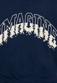 Felpa blu navy con grafica bianca "IMAGINE". Il testo presenta un design sfumato pixelato. Tessuto morbido, collo rotondo e orlo a coste.