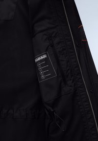 Black jacket interior showing mesh lining, zippered pocket with brand label detailing taped seams, breathable, ripstop, and water-resistant fabric.