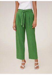 Zelené lněné kalhoty s širokými nohavicemi a páskem na zavázání, s plisováním a hladkou texturou. Kombinované s bílými sandály na zavazování.