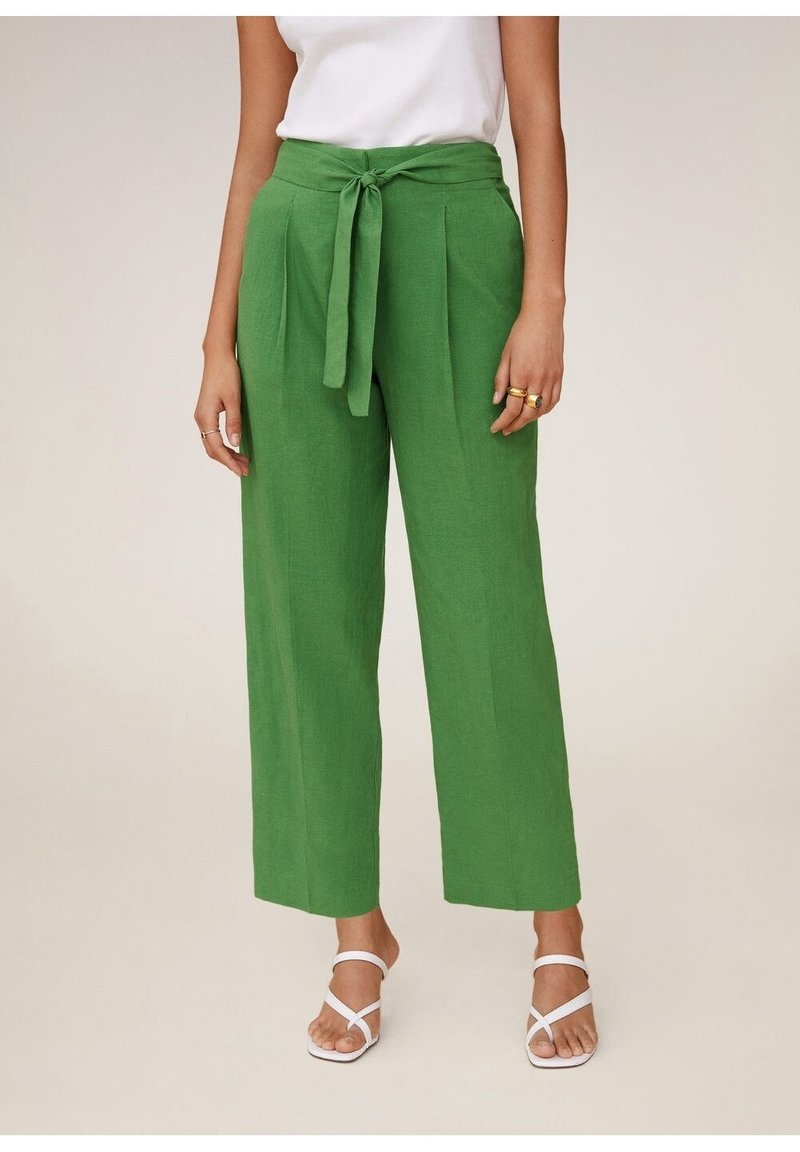 Zelené lněné kalhoty s širokými nohavicemi a páskem na zavázání, s plisováním a hladkou texturou. Kombinované s bílými sandály na zavazování.