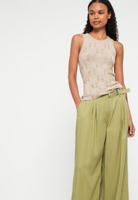 Μπεζ πλέκτο τοπ με υφασμάτινο σχέδιο, συνδυασμένο με χαλαρές ελαιοπράσινες παντελόνες που διαθέτουν ζωνάκι στη μέση και πλαϊνές τσέπες.