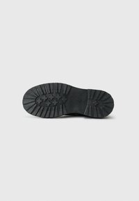Suela de zapato de goma negra con un patrón de tracción texturizado, que presenta diseños circulares y cruzados para mayor agarre y tracción. Forma plana y robusta.