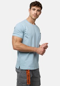 Himmelblaues Baumwoll-T-Shirt mit kurzen Ärmeln und Rundhals. Verfügt über eine kleine Brusttasche und Seitenschlitze am Saum.