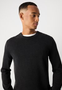 Schwarzer gestrickter Pullover mit rundem Hals, strukturiertem Stoff und langen Ärmeln. Verfügt über einen gerippten Halsausschnitt und dezente Details.