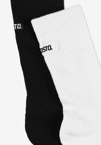 Czarno-białe prążkowane skarpetki do kostki z małą metką z logo. Czarna skarpetka po lewej, biała po prawej.