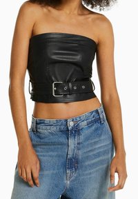 Top corto sin mangas de cuero negro con cintura ceñida; textura suave con detalles de costura visibles, combinado con jeans de mezclilla azul claro.