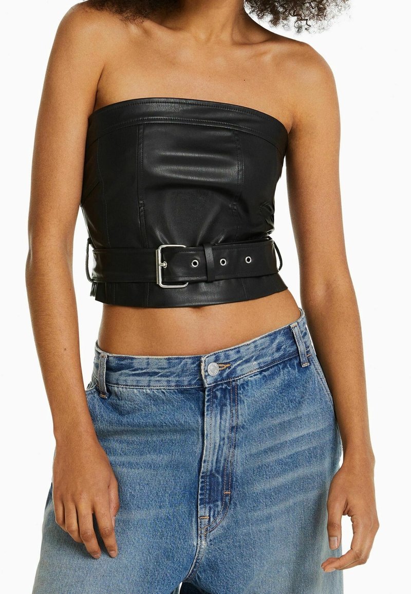 Top corto sin mangas de cuero negro con cintura ceñida; textura suave con detalles de costura visibles, combinado con jeans de mezclilla azul claro.