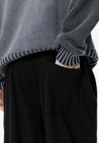 Szary sweter dzianinowy z prążkowanymi mankietami i dolnym obszyciem, w zestawieniu z teksturowanymi czarnymi spodniami z bocznymi kieszeniami. Skupienie na detalach tkaniny i sylwetki.